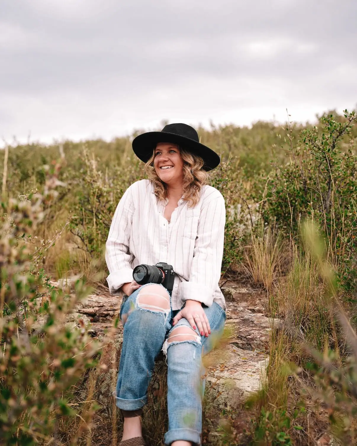 Delaney Ireland sitting on a rock outcrop in an open Colorado field, camera in her lap