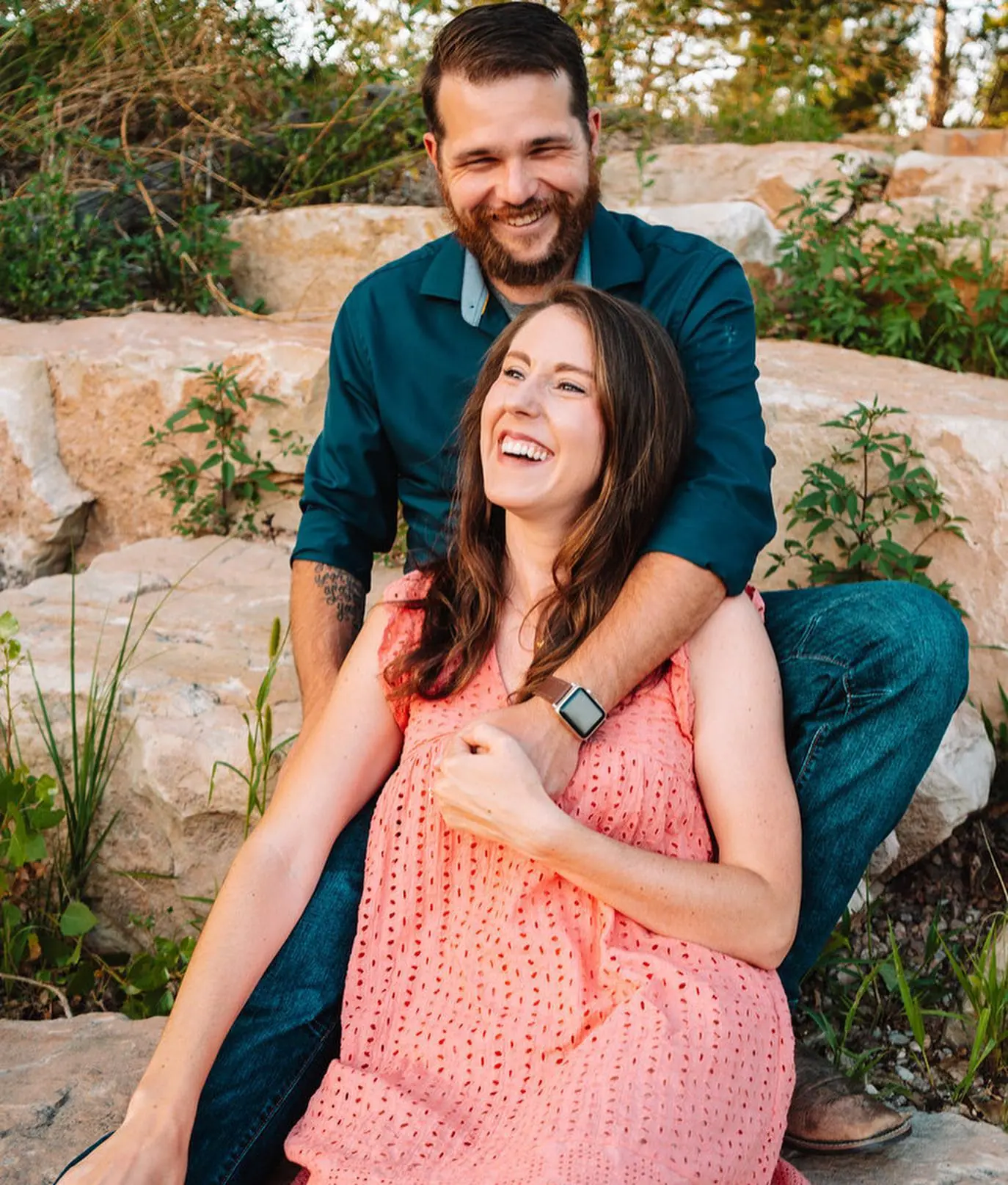 A couple laughing together on sandstone boulders at golden hour