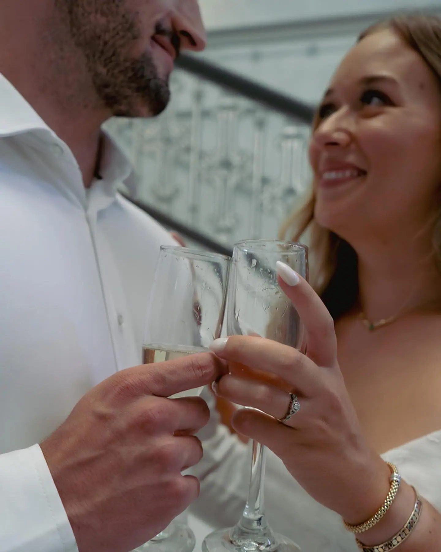 A couple clinking champagne glasses, her engagement ring catching the light